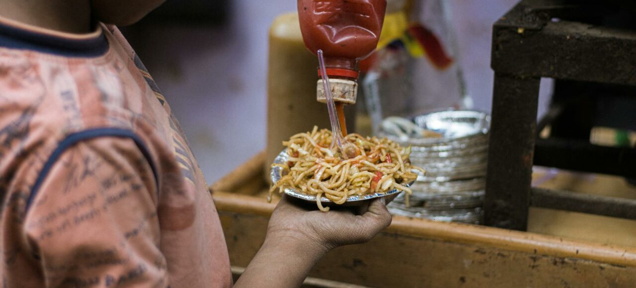 child putting ketchup on pasta