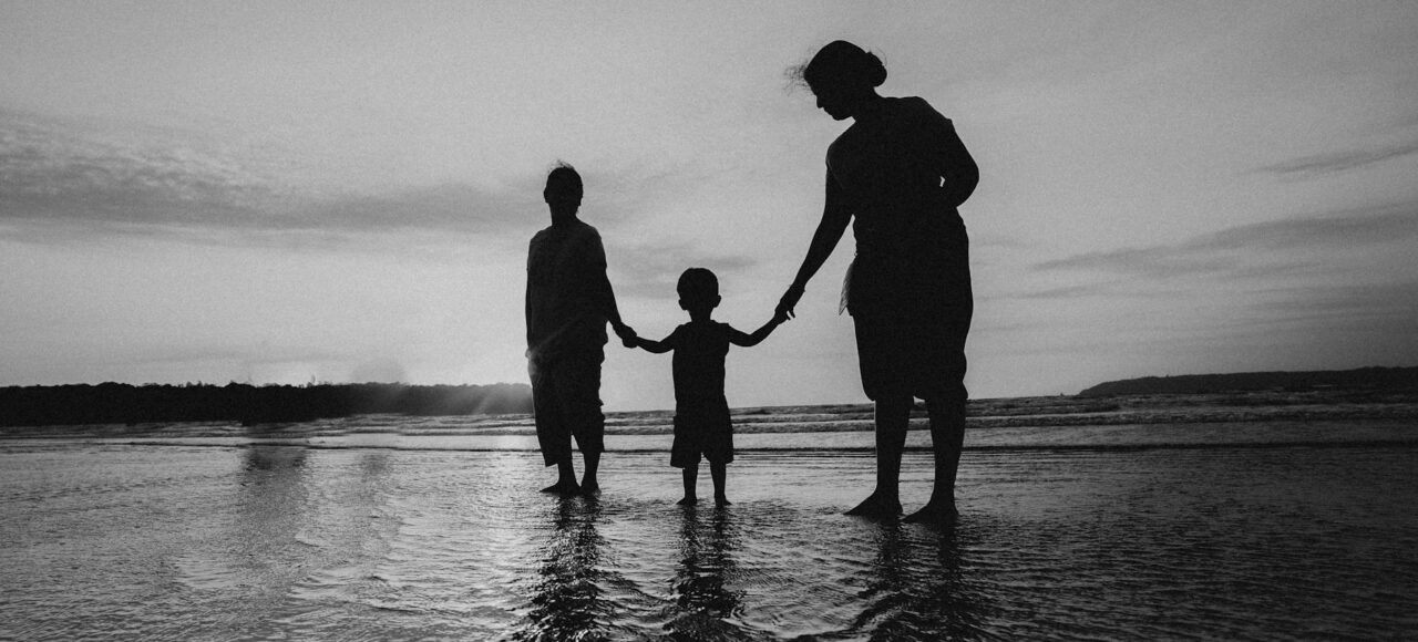 monochrome photo of people holding hands while standing on beach