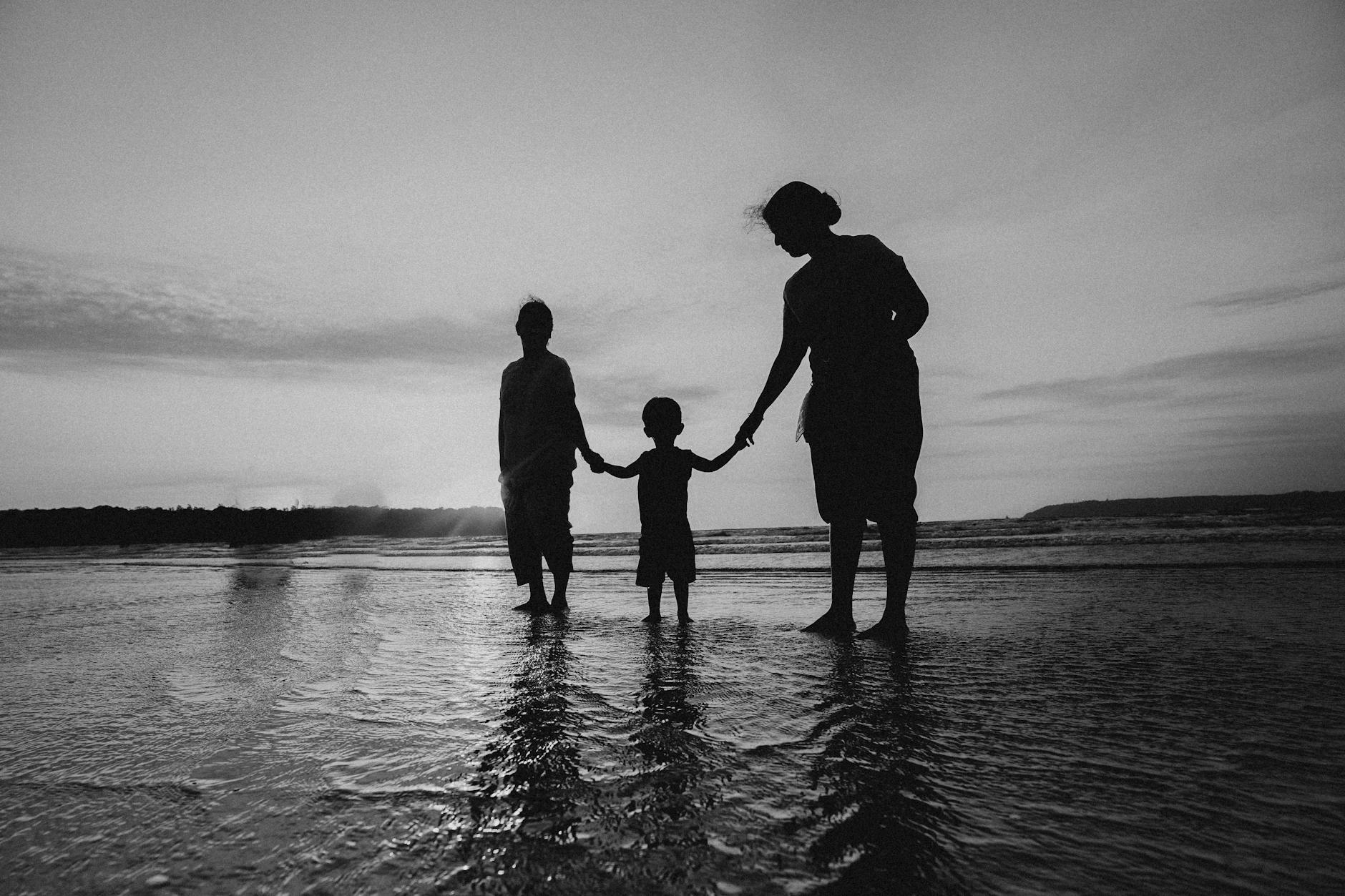 monochrome photo of people holding hands while standing on beach
