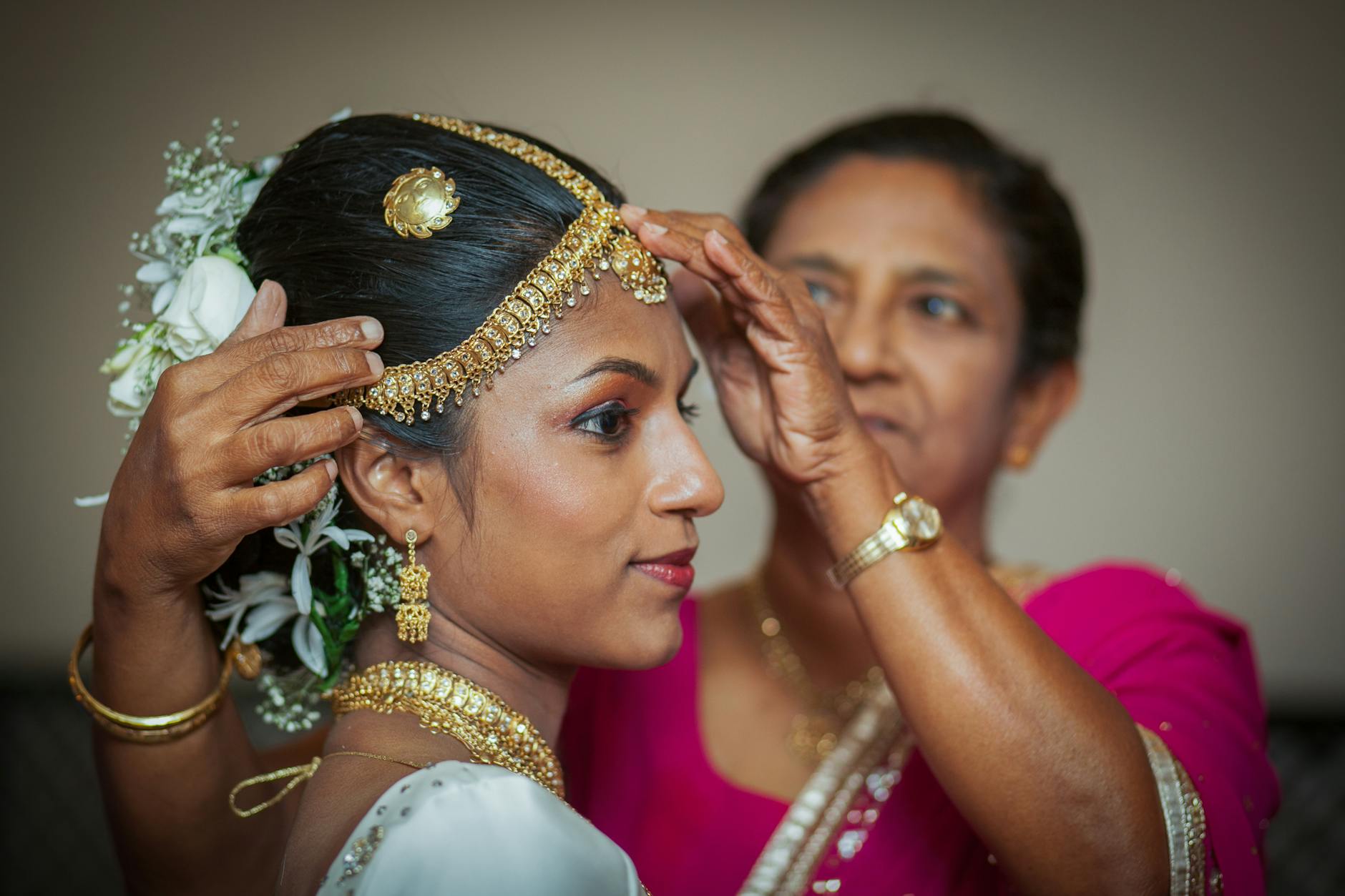ethnic woman putting traditional jewelry on head of young sinhalese bride