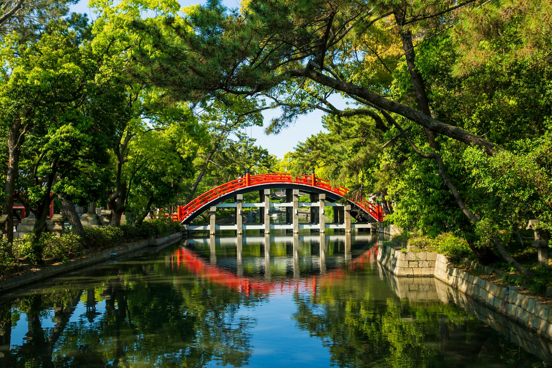 aged red bridge above water channel near trees in park